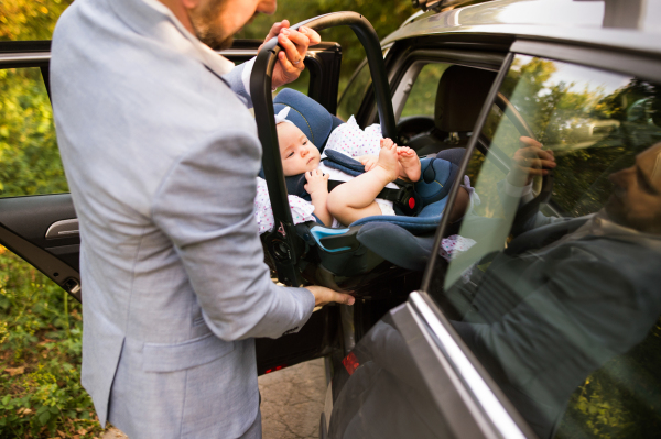 Unrecognizable man putting car seat with a baby girl in the car.