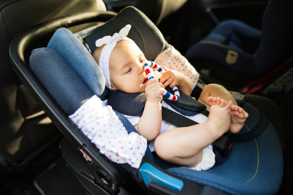 Cute little baby girl fastened with security belt in safety car seat.