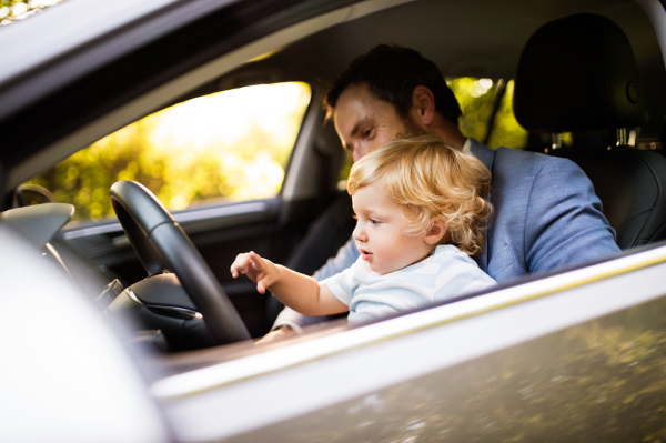 Man driving a car with little son. Toddler boy sitting in his fathers lap.