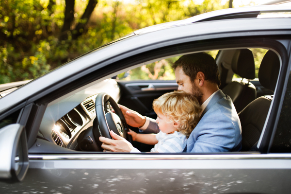 Man driving a car with his little son. Toddler boy sitting in his fathers lap.