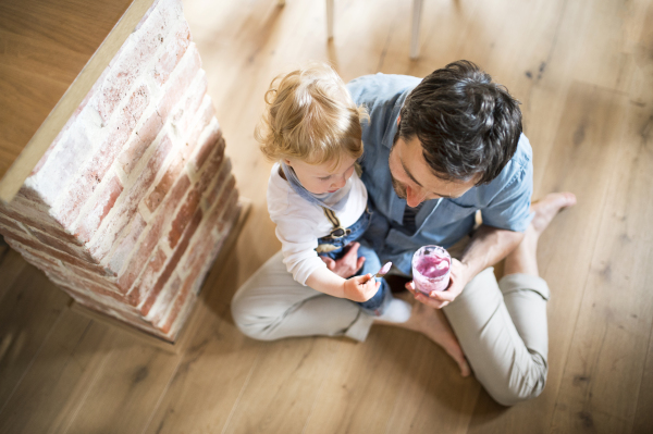 Young father with his son at home eating yoghurt.