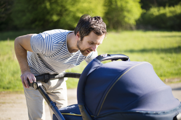 Young father outside on walk with his baby in park.