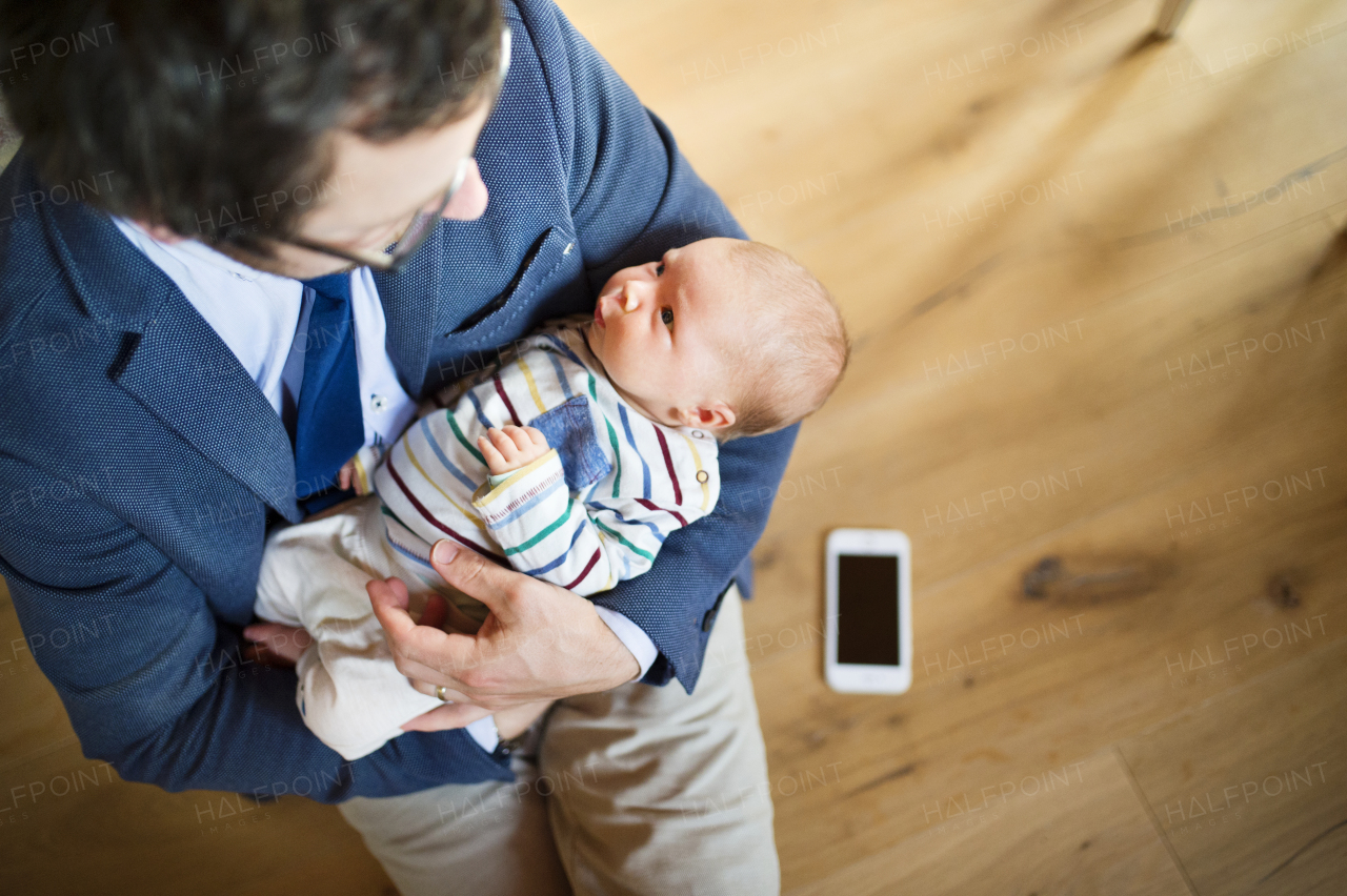 Young businessman at home with his little baby daughter in the arms. Smart phone laid on wooden floor.