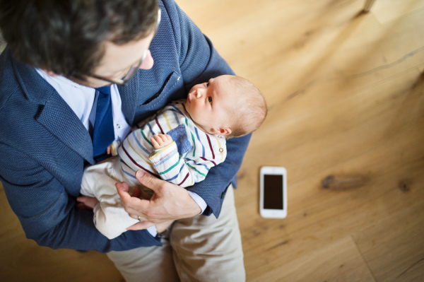 Young businessman at home with his little baby daughter in the arms. Smart phone laid on wooden floor.