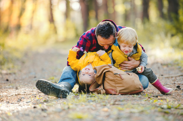 A mature father with backpack and toddler son in an autumn forest, resting.