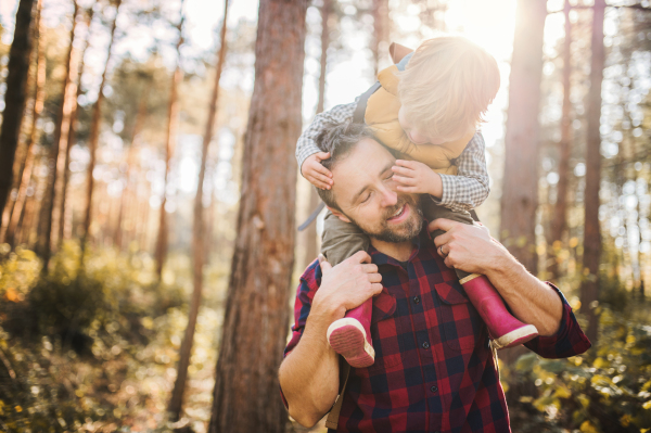 A mature father giving a toddler son a piggyback ride in an autumn forest, having fun.