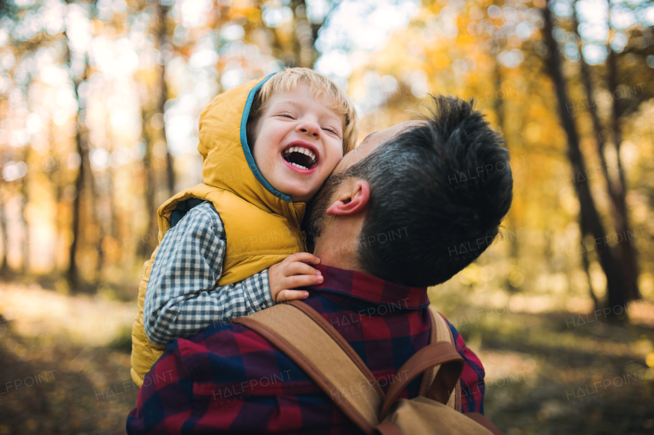 A mature father standing and holding a toddler son in an autumn forest, having fun.