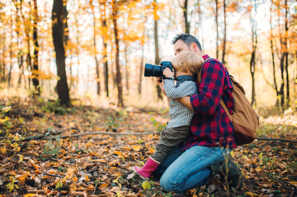 A mature father and a toddler son in an autumn forest, taking pictures with a digital camera.