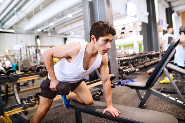 Young hispanic fitness man in gym on bench, working out with weights