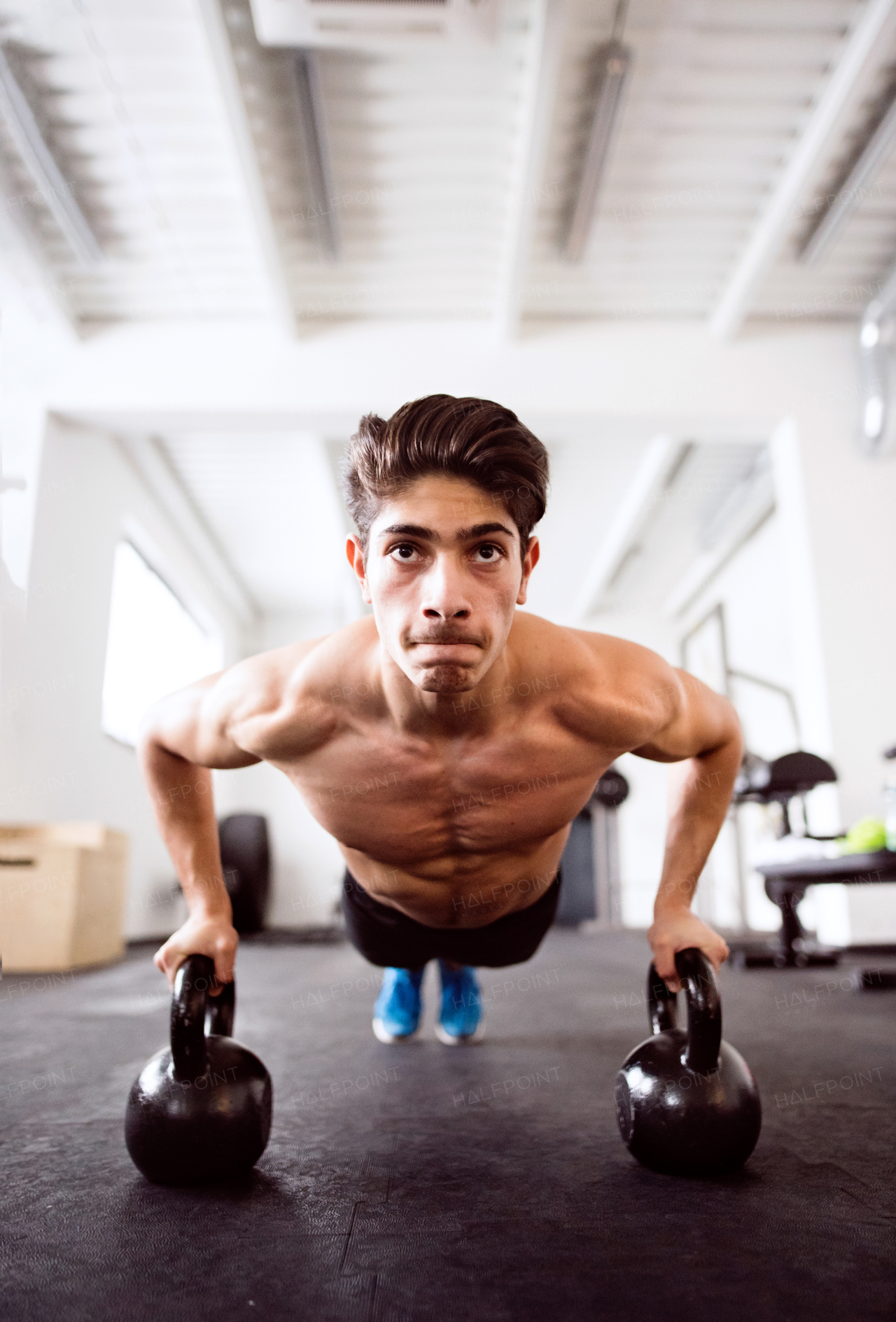 Fit hispanic man doing strength training, doing push ups on kettlebells in crossfit gym