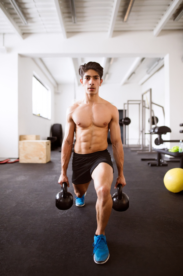 Fit hispanic man doing strength training, doing lunges with kettlebells in crossfit gym