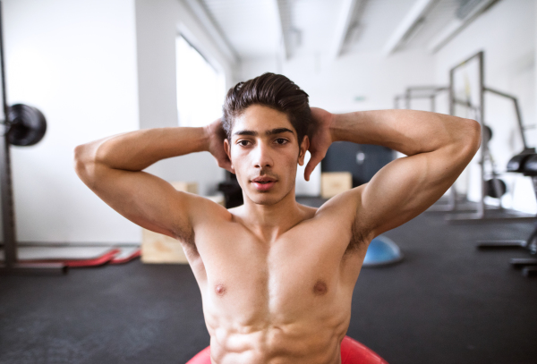 Fit hispanic man at abdominal crunch muscles exercises on fitness ball during training in fitness gym.