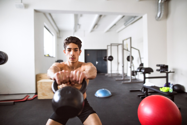 Fit hispanic man doing strength training, doing kettlebell swings in crossfit gym