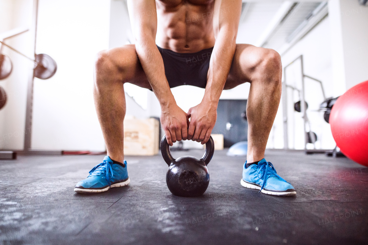 Unrecognizable young fit man doing strength training, doing squats with kettlebell in crossfit gym