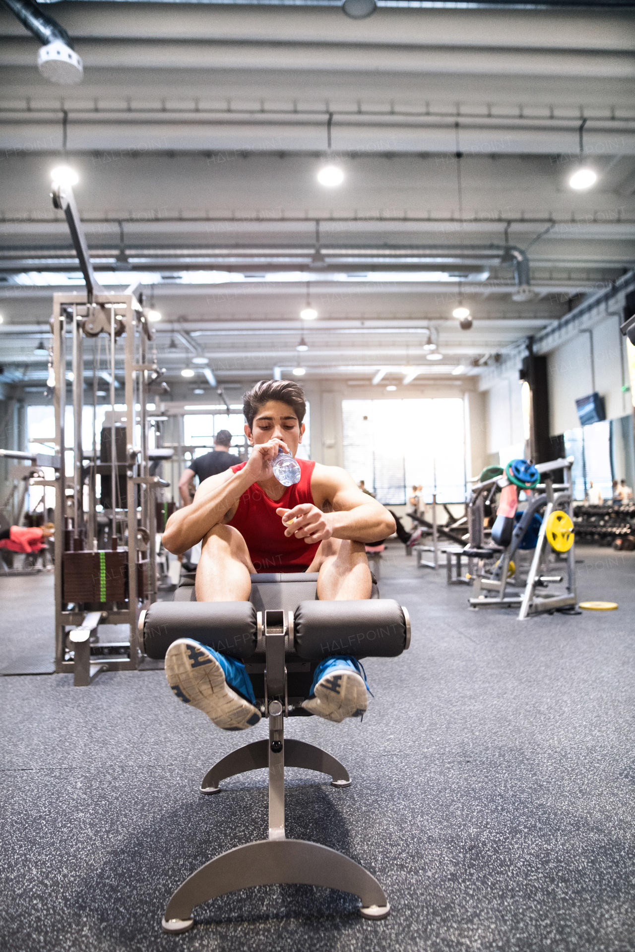 Hispanic fitness man resting on the bench in gym, drinking water