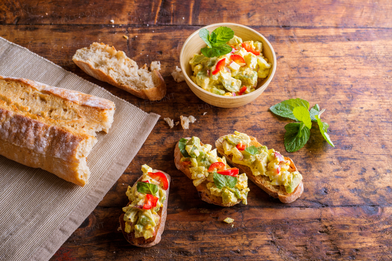 Spread made of avocado and other ingredients in a bowl and on slices of bruschetta. Studio shot on old wooden table background