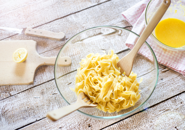 Glass bowl full of tagliatelle laid on a wooden table