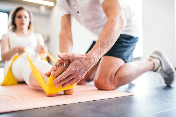 Unrecognizable senior male physiotherapist working with a young female patient.