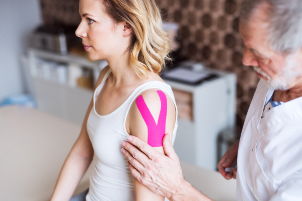 Senior male physiotherapist applying tape on a young female patient.