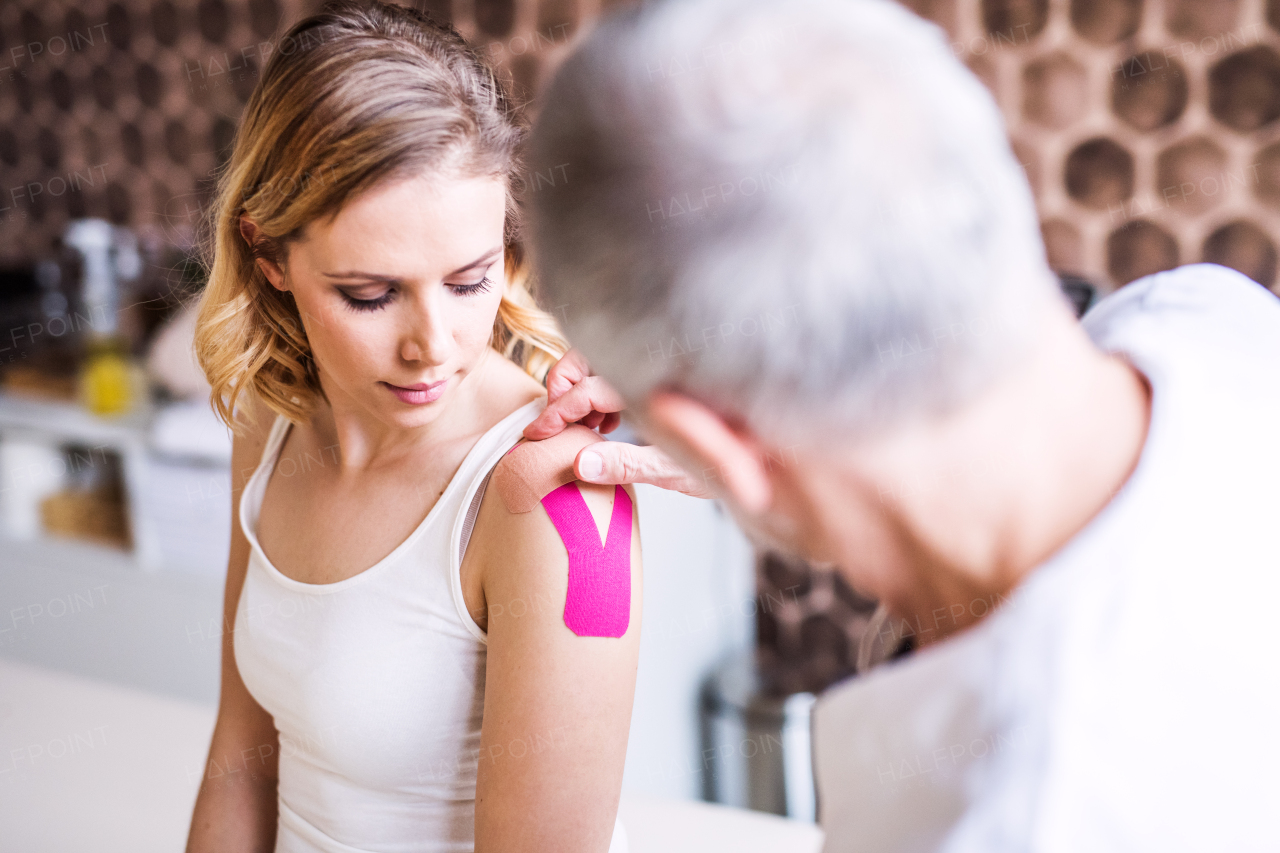 Senior male physiotherapist applying tape on a young female patient.