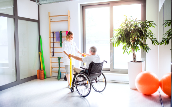 Young attractive woman physiotherapist working with a senior man in wheelchair.