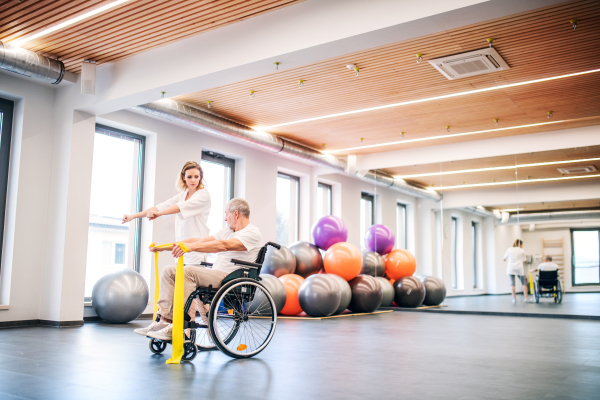 Young attractive woman physiotherapist working with a senior man in wheelchair.