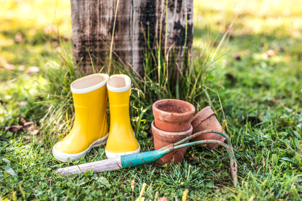 Hoe, wellington boots and flower pots on the grass in the garden.