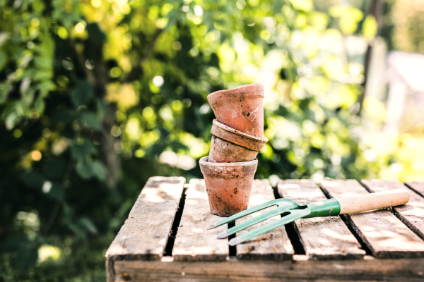 Close up of garden tools in the garden. Hand fork and flower pots on the wooden table.