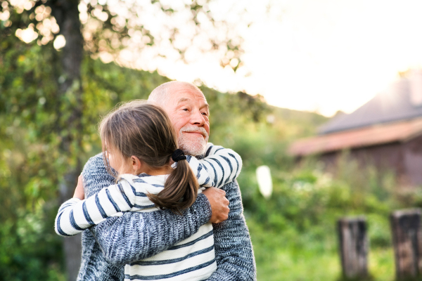 Grandfather giving his grandaughter a hug. Senior man and a small girl enjoying time in nature.