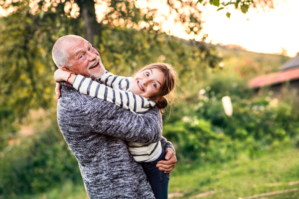 Grandfather giving his granddaughter a hug. Senior man and a small girl enjoying time in nature, having fun.