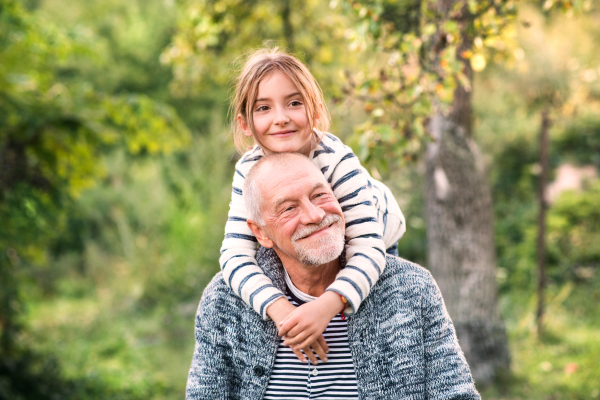 Grandfather carrying his grandaughter on his shoulders. Senior man and a small girl enjoying time in nature.