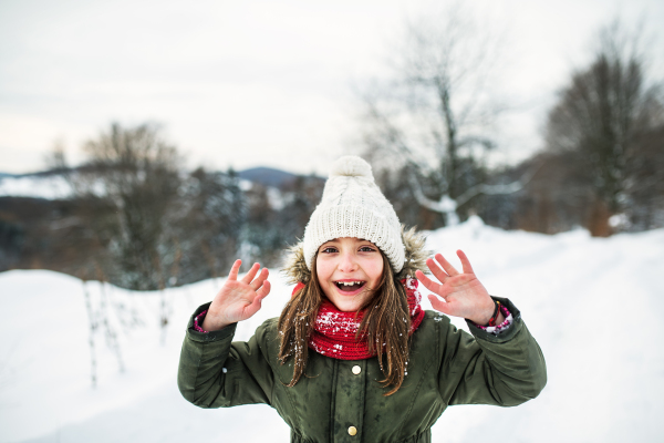 Waist-up portrait of a small girl in winter nature, wearing coat, hat and scarf.