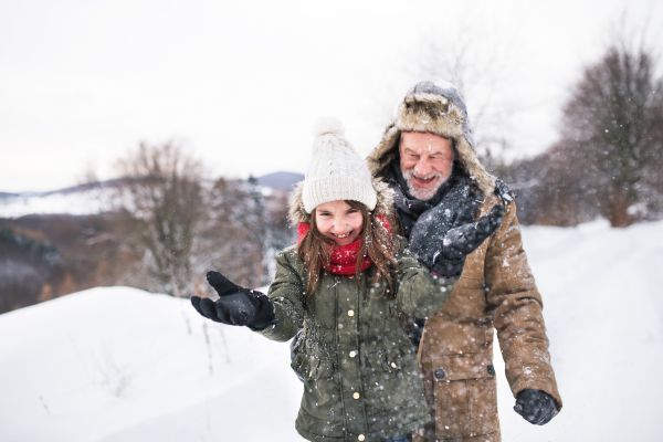 Senior grandfather and a small girl having fun in snow on a winter day.