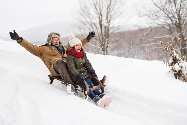 Senior grandfather and a small girl sledging, having fun. Winter day.