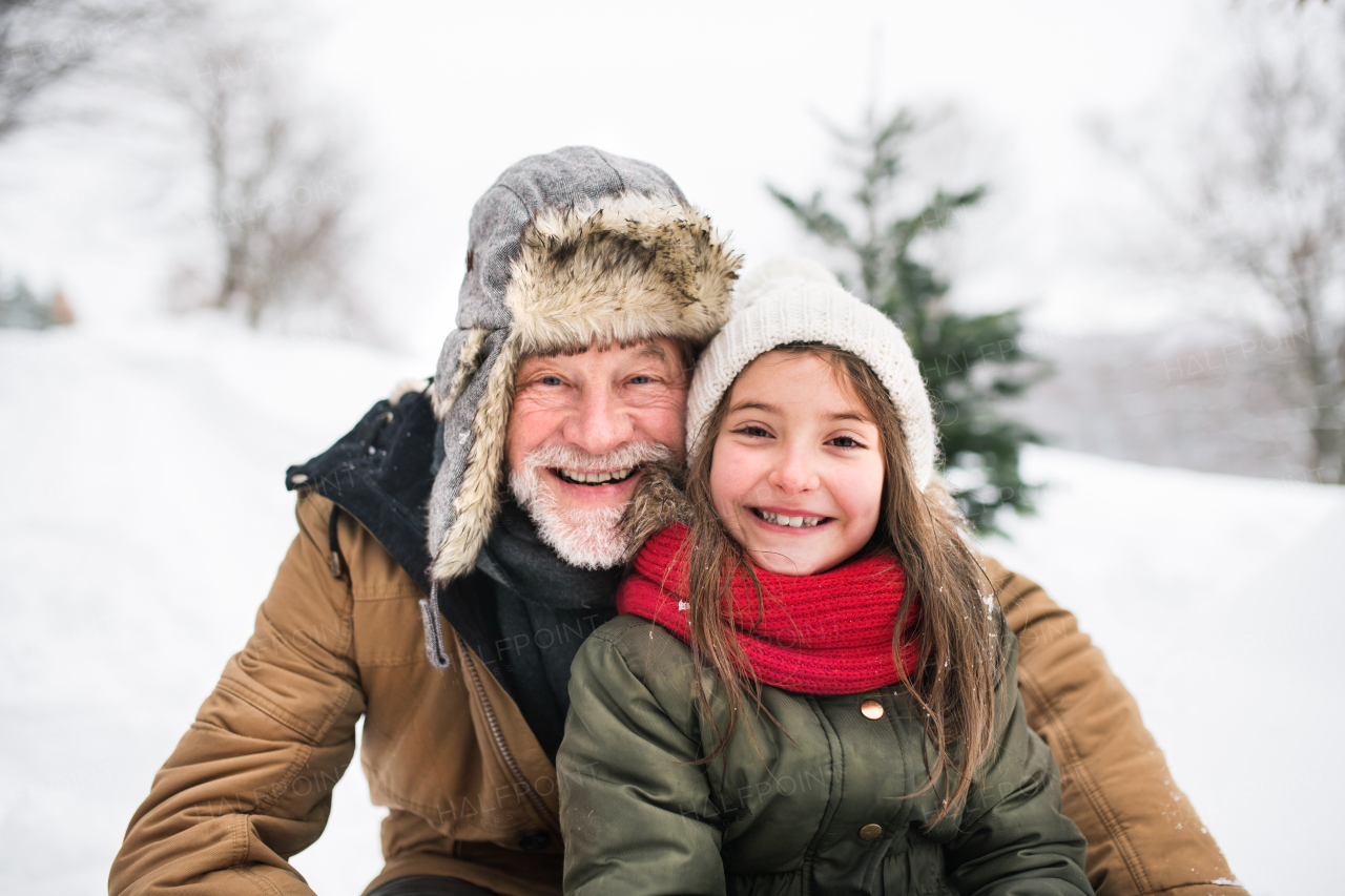 Senior grandfather and a small girl having fun in snow on a winter day.