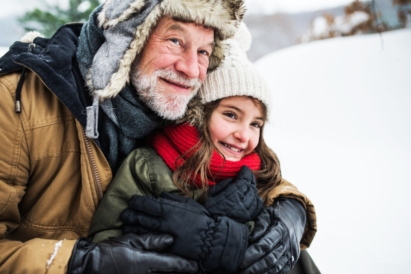 A portrait of senior grandfather and a small girl in snowy nature on a winter day.