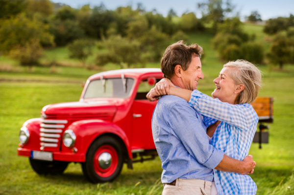 Senior couple hugging, vintage styled red car, green sunny nature