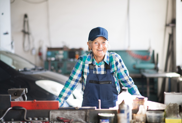 Female mechanic repairing a car. A senior woman standing in a garage.