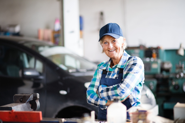 Female mechanic repairing a car. A senior woman standing in a garage, arms crossed.