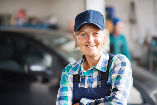 Female mechanic repairing a car. A senior woman standing in a garage, arms crossed.