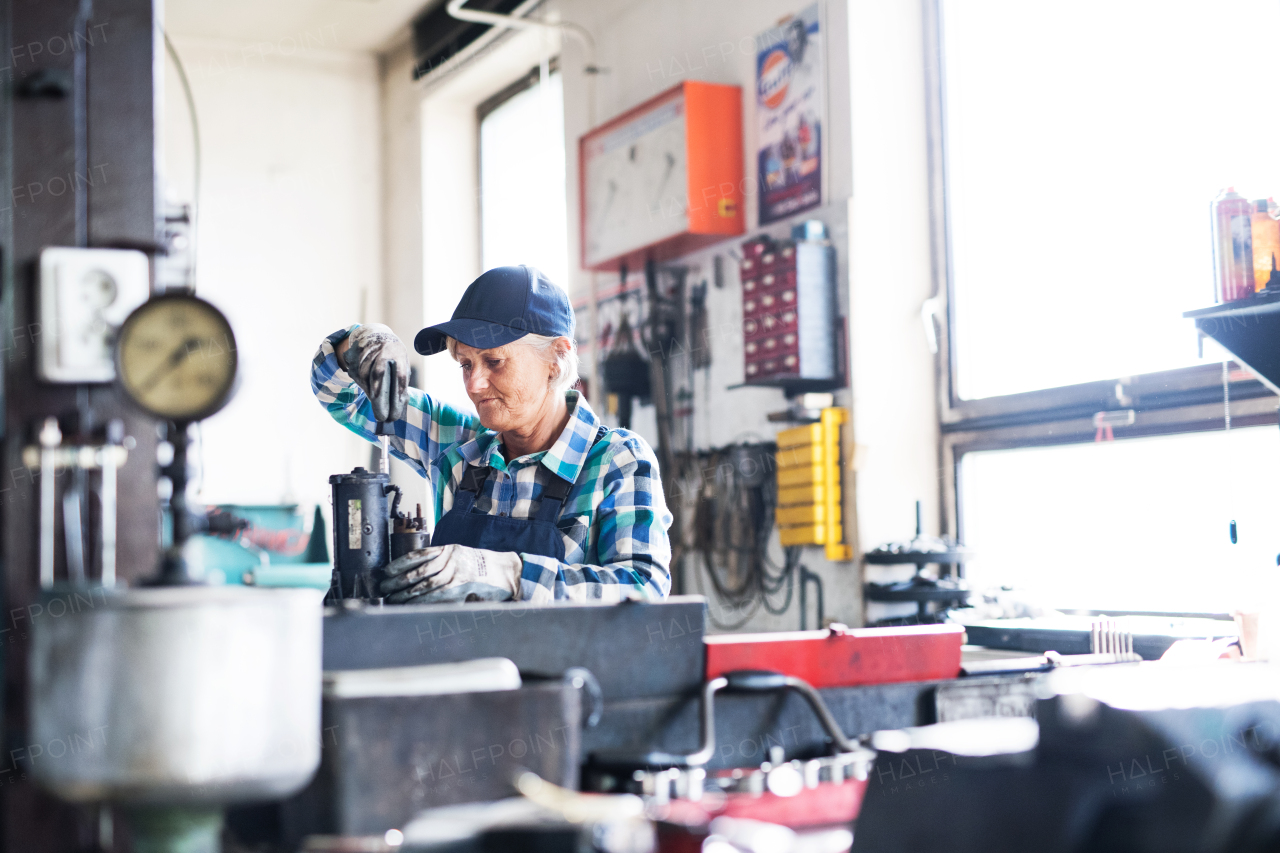 Female mechanic repairing a car. A senior woman working in a garage.