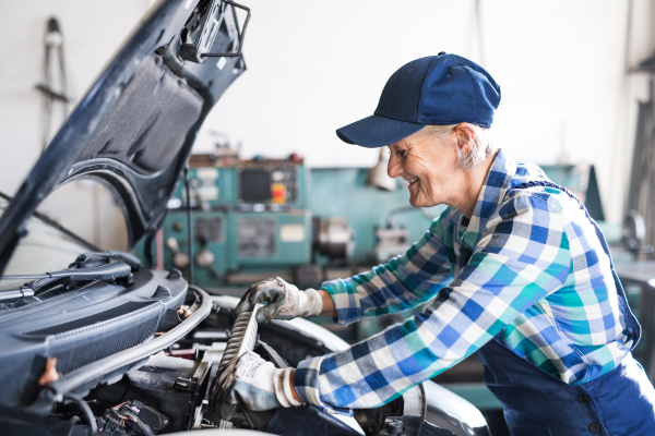 Female mechanic repairing a car. A senior woman working in a garage.