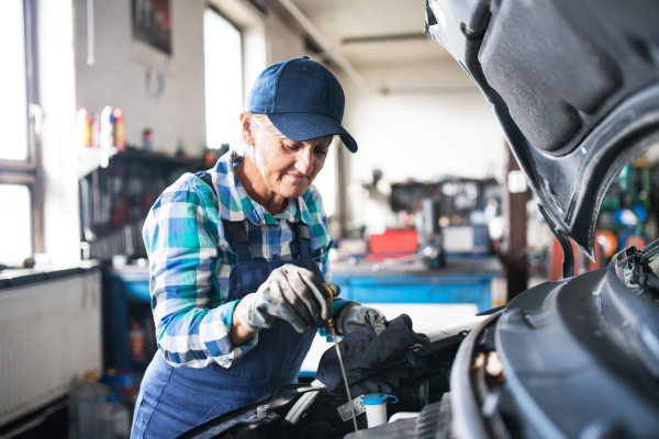 Female mechanic repairing a car. A senior woman working in a garage.