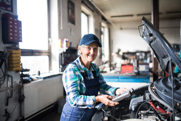 Female mechanic repairing a car. A senior woman working in a garage.