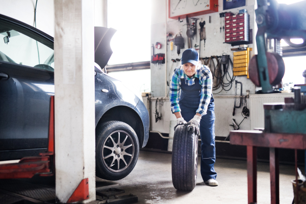 Female mechanic repairing a car. A senior woman working in a garage.