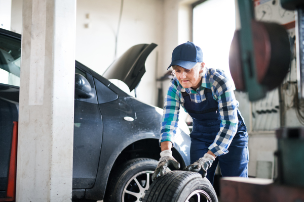 Female mechanic repairing a car. A senior woman working in a garage.