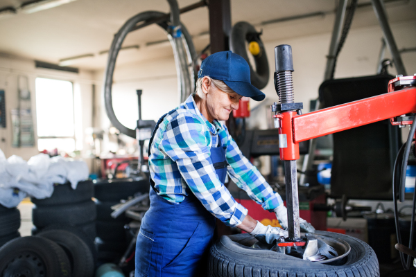 Female mechanic repairing a car. A senior woman working in a garage.