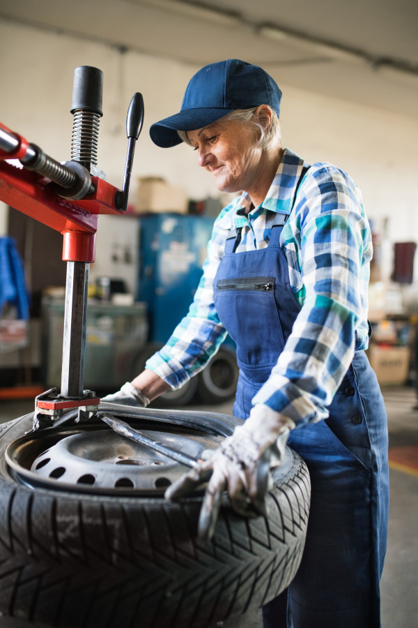 Female mechanic repairing a car. A senior woman working in a garage.