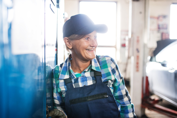 Female mechanic repairing a car. A senior woman standing in a garage, arms crossed.