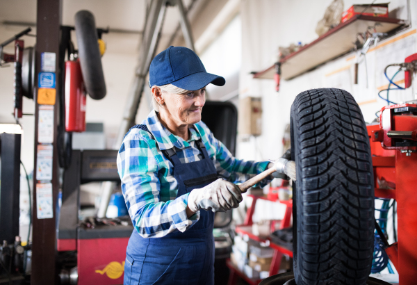 Female mechanic repairing a car. A senior woman working in a garage.